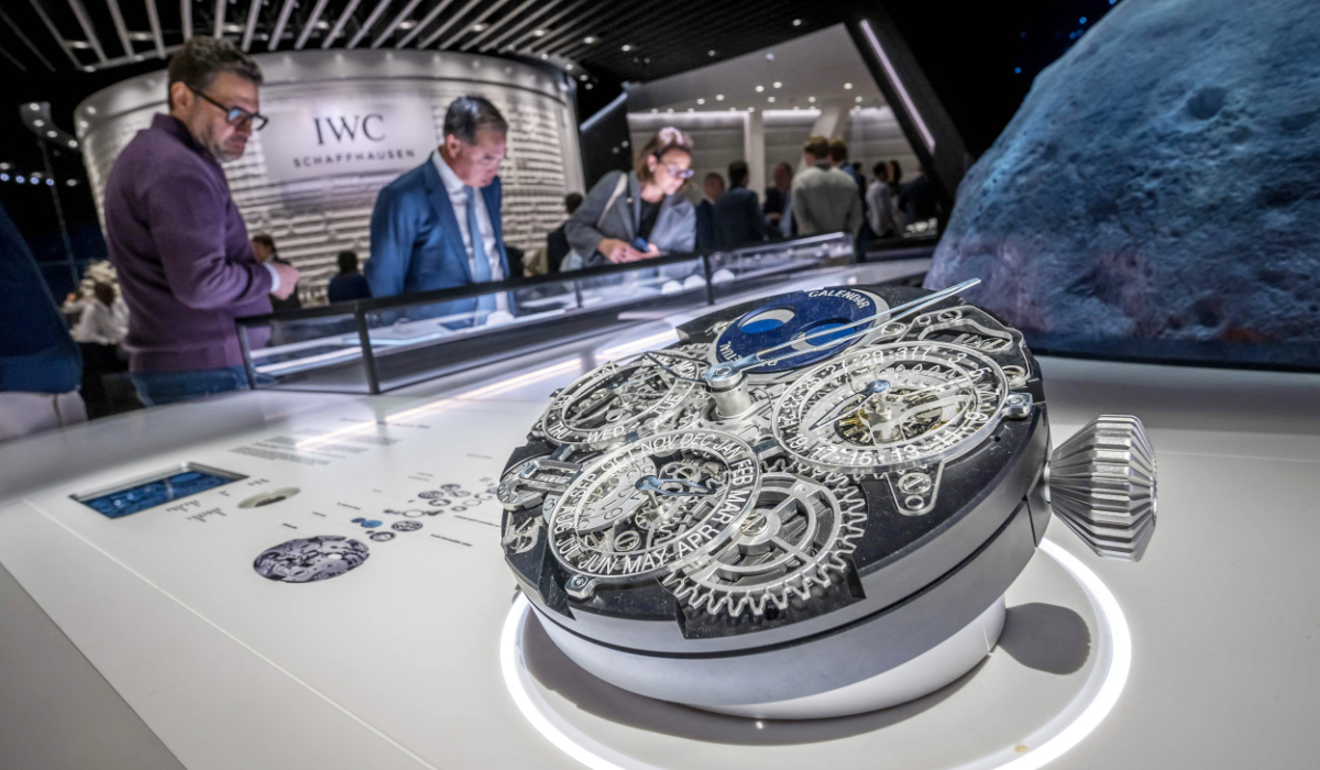 Visitors look at a replica of a watch depicting its movement mechanisms displayed at the stand of Swiss luxury watchmaker IWC, owned by the Richemont group, on the opening day of the Watches and Wonders Geneva luxury watch fair, in Geneva on April 14, 2026. (AFP)