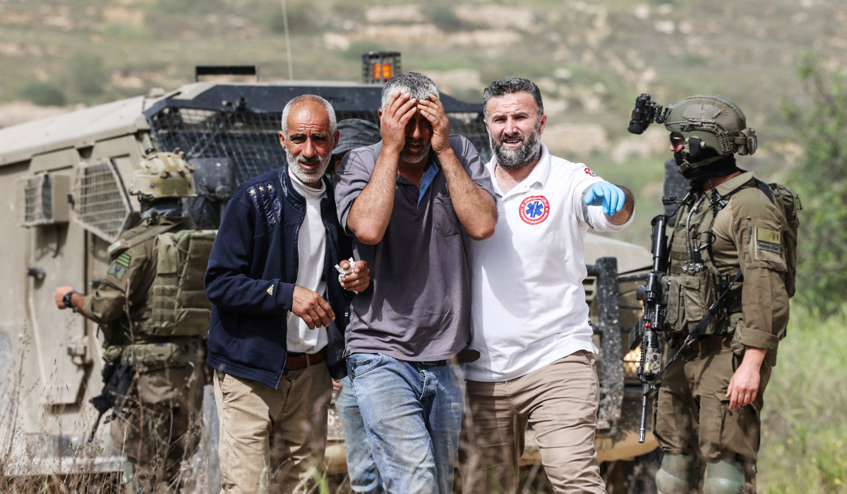 Israeli soldiers stand by as Palestinian medics assist a man who was reportedly attacked with pepper spray by Jewish settlers while he worked on his farmland near the Palestinian village of Halhoul, south of the Israel-occupied West Bank city of Hebron, on April 17, 2026. (AFP)