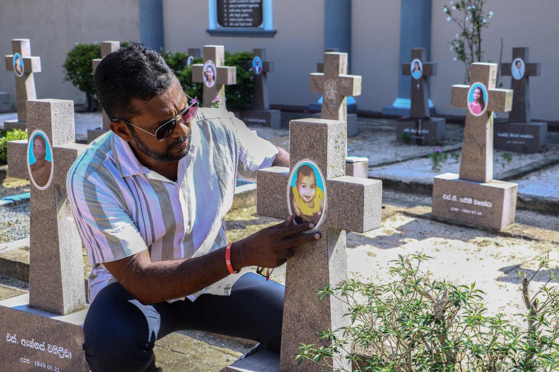This photograph taken on April 17, 2026 shows Dinal Fernando, a marketing executive who survived the 2019 Sri Lanka Easter bombings, sitting near the grave of an eight-month-old infant who was killed in the attacks, at the St. Sebastian's Church in the Katuwapitiya village of the country's coastal town of Negombo. (Photo by AFP)