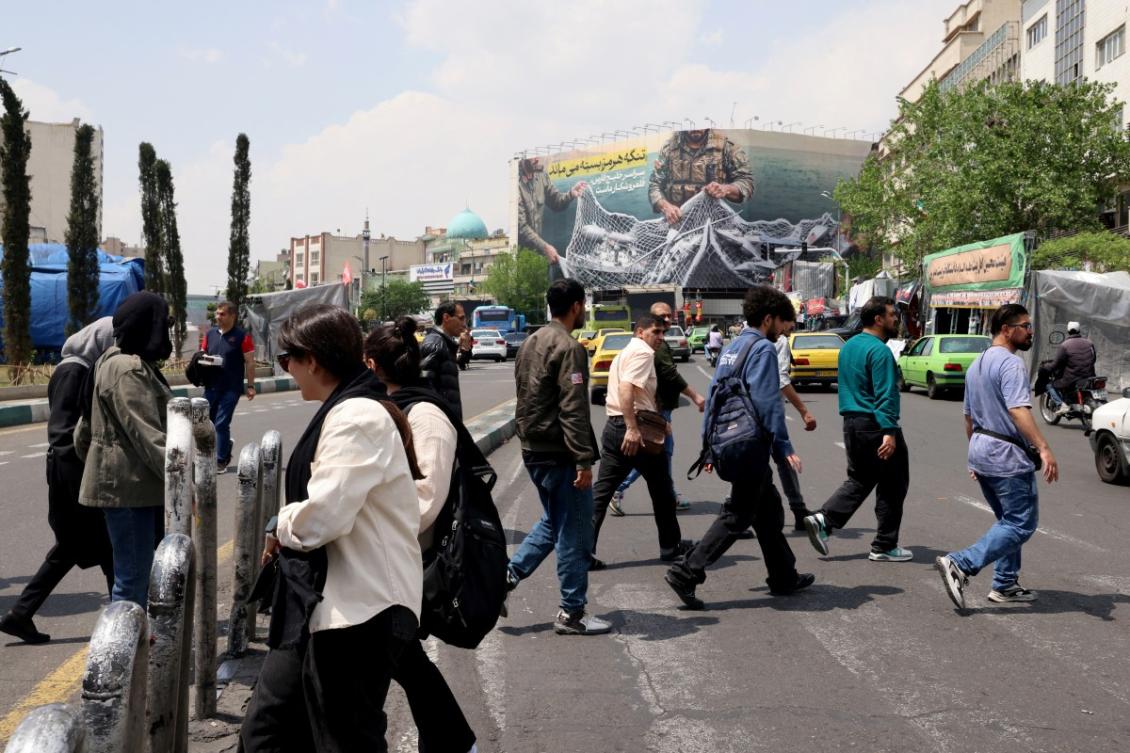 Iranians walk across a zebra crossing past a giant billboard reading 'The Strait of Hormuz remains closed' at the Revolution Square in Tehran on April 22, 2026. (File/AFP)