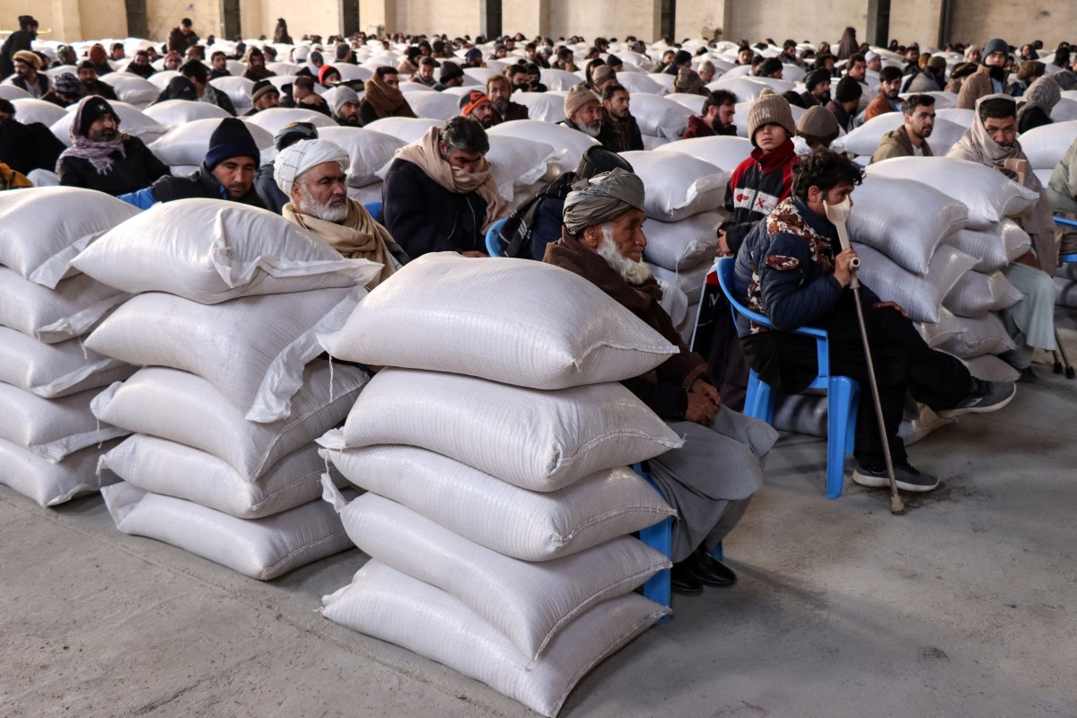 Afghan migrants recently returned from Iran receive sacks of wheat aid distributed by Afghanistan's Ministry of Agriculture in Herat, Afghanistan. (AFP)