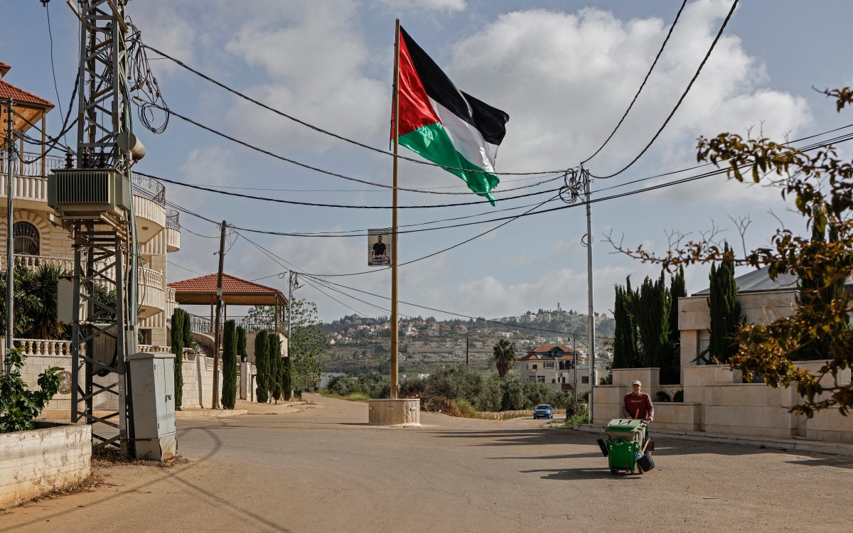 A worker walks past a Palestinian flag installed along a street in Turmus Ayya village, north of Ramallah, in the Israeli-occupied West Bank, April 19, 2026. (Files / AFP)