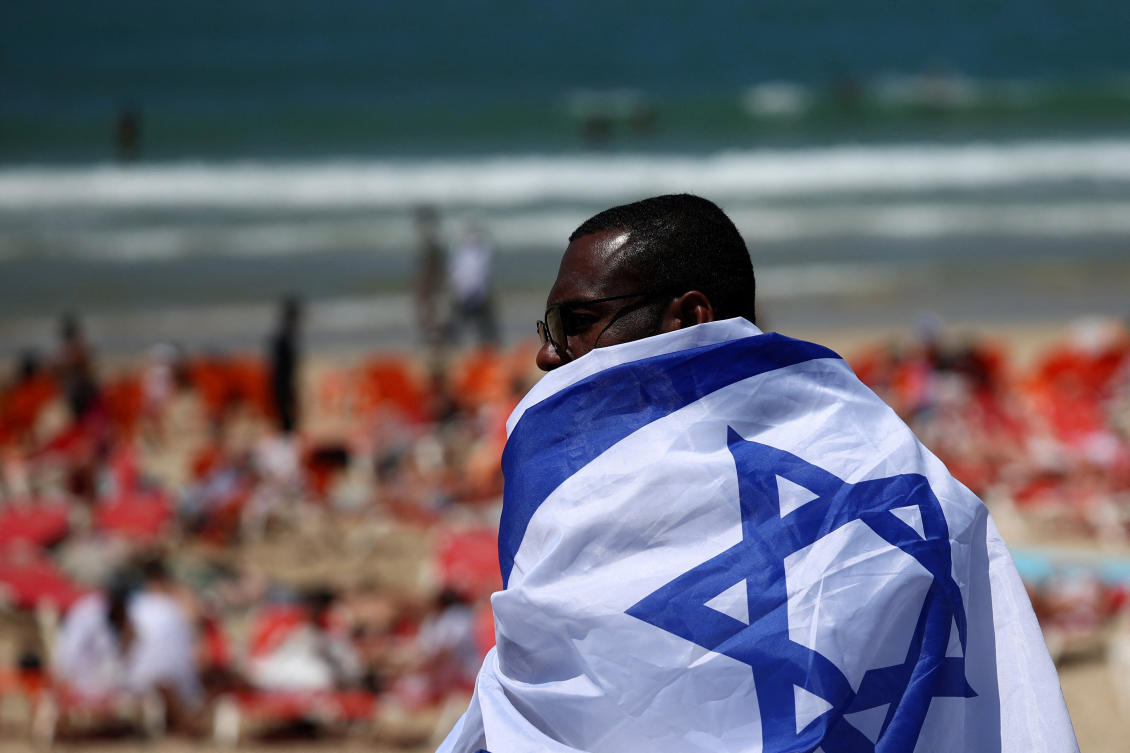 A man wrapped in an Israeli flag sits by the beach on Israel’s 78th Independence Day in Tel Aviv, Israel, April 22, 2026. (Reuters)