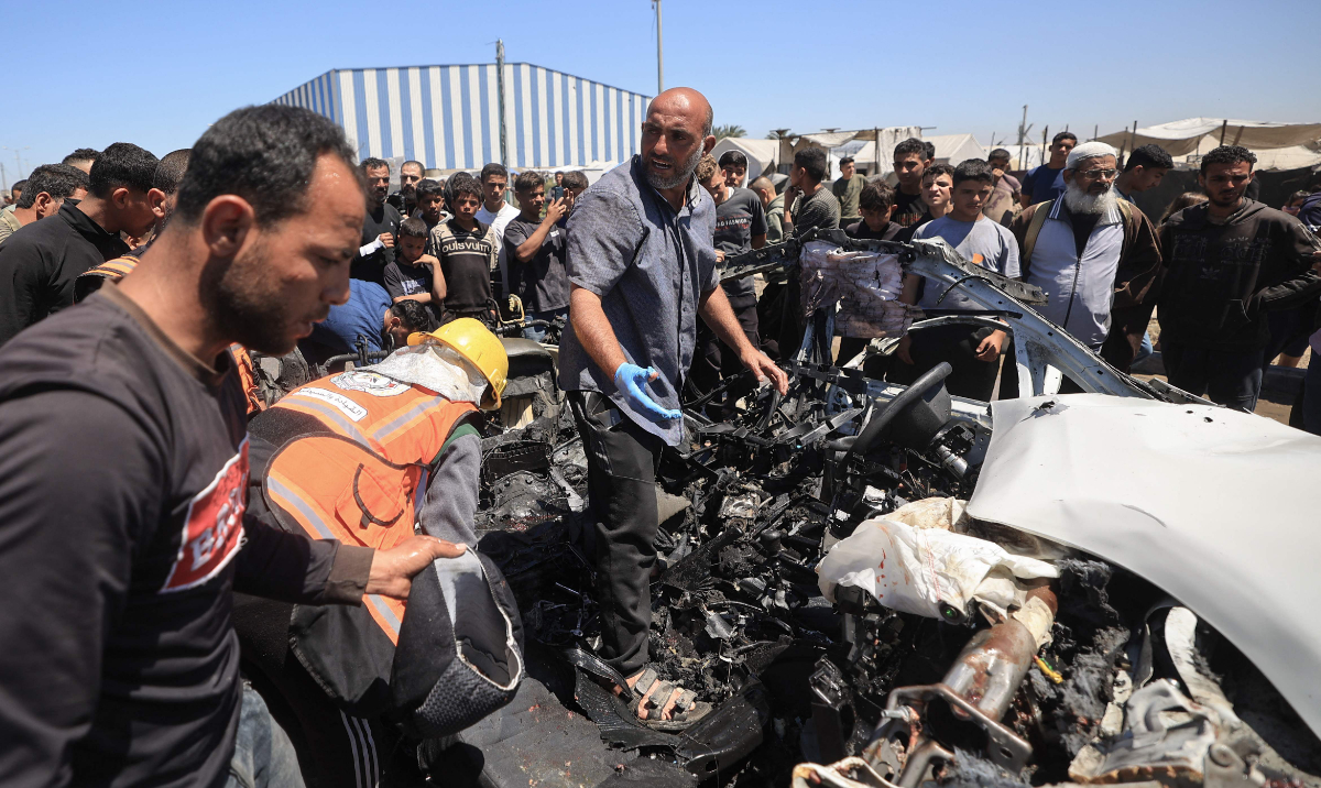 People inspect a destroyed civilian vehicle after it was targeted by an Israeli airstrike on Salah Al-Din Street, south of Al-Bureij camp for Palestinian refugees in the central Gaza Strip. (AFP)