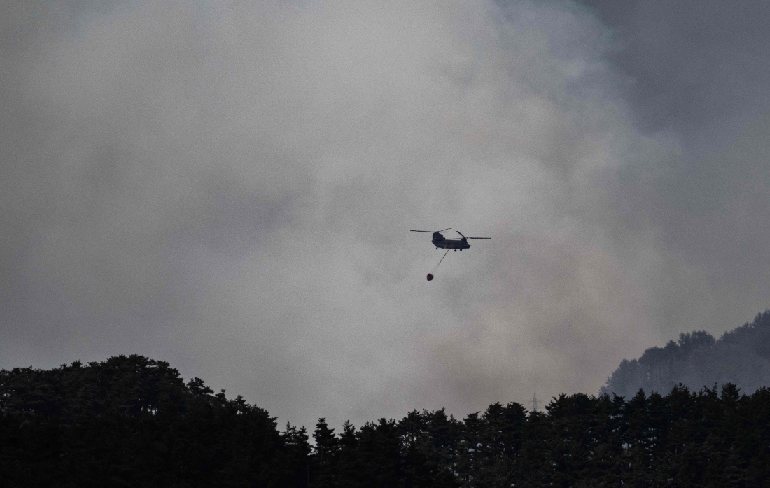 A helicopter doing water drops flies over smoke from a forest fire near the town of Otsuchi, in Iwate Prefecture, Japan. (AFP)