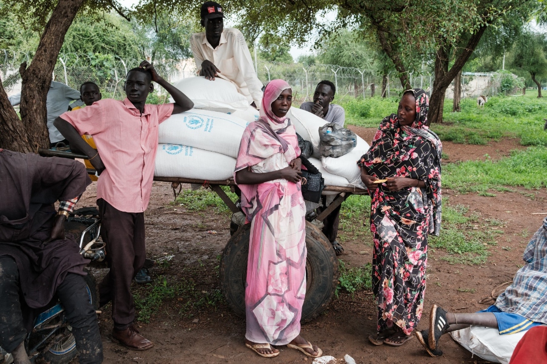 People wait outside a food distribution site as large bags of sorghum are prepared to be taken back to refugee camps in Maban, South Sudan. (AFP)