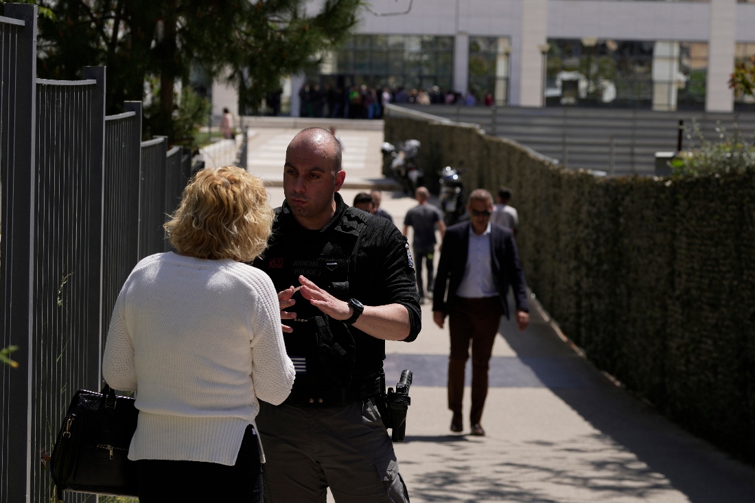 A policeman speaks with a woman outside a courthouse after a gunman opened fire leaving several people wounded in Athens, Greece. (AP)