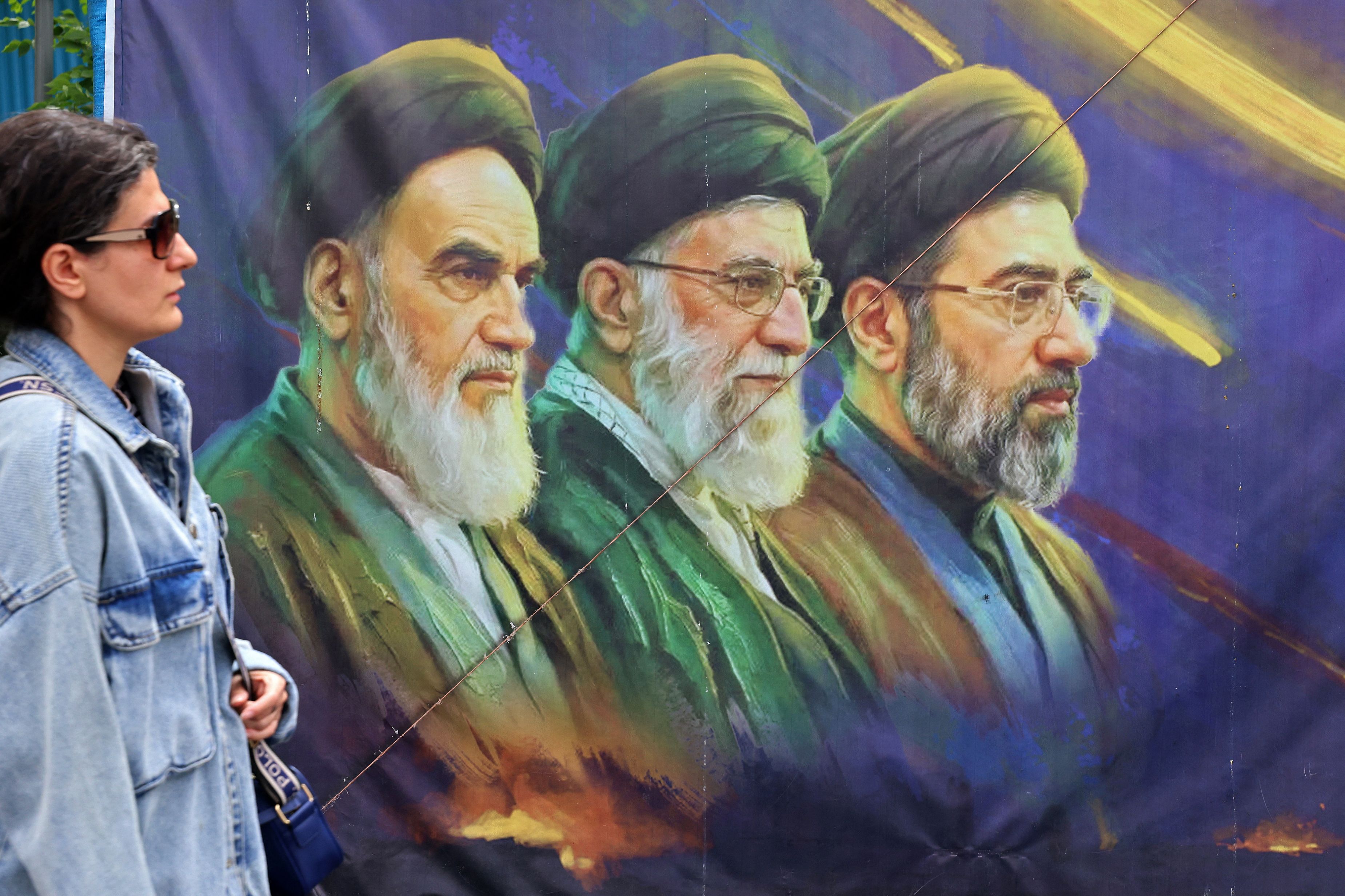 A woman walks past a banner featuring Iran's late supreme leaders. (AFP)