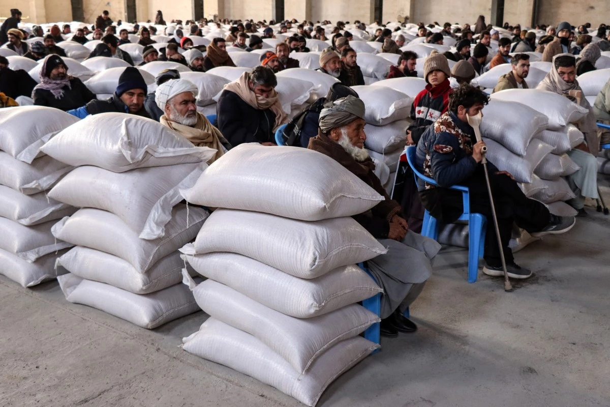 Afghan migrants recently returned from Iran receive sacks of wheat aid distributed by Afghanistan's Ministry of Agriculture in Herat, Afghanistan. (AFP)