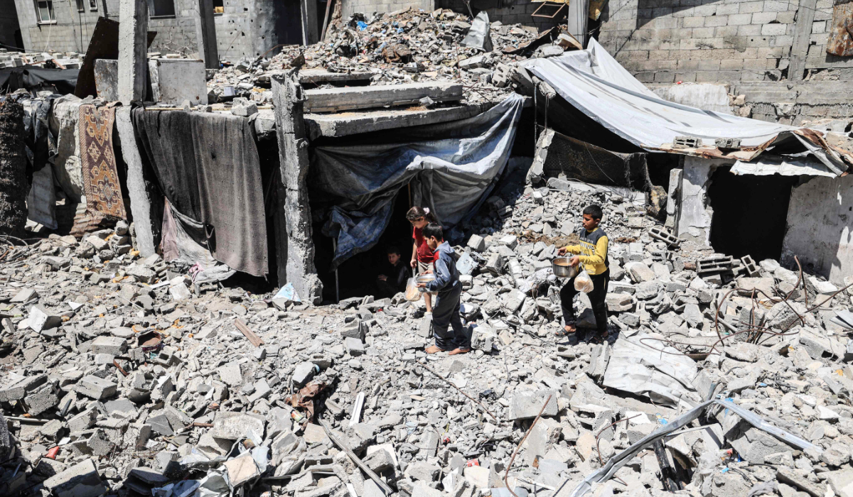 Displaced Palestinian children carry pots of food collected from a charity kitchen to their family shelter beneath the rubble of buildings destroyed by the Israeli military, in the Bureij refugee camp in the central Gaza Strip on May 1, 2026. (AFP)