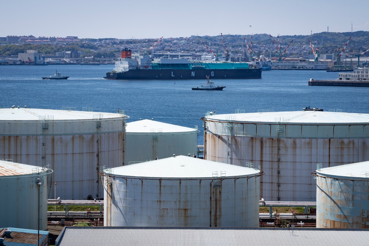 A liquefied natural gas (LNG) tanker sails past oil storage tanks at an oil refinery in Yokohama, Kanagawa, Japan. (AFP)