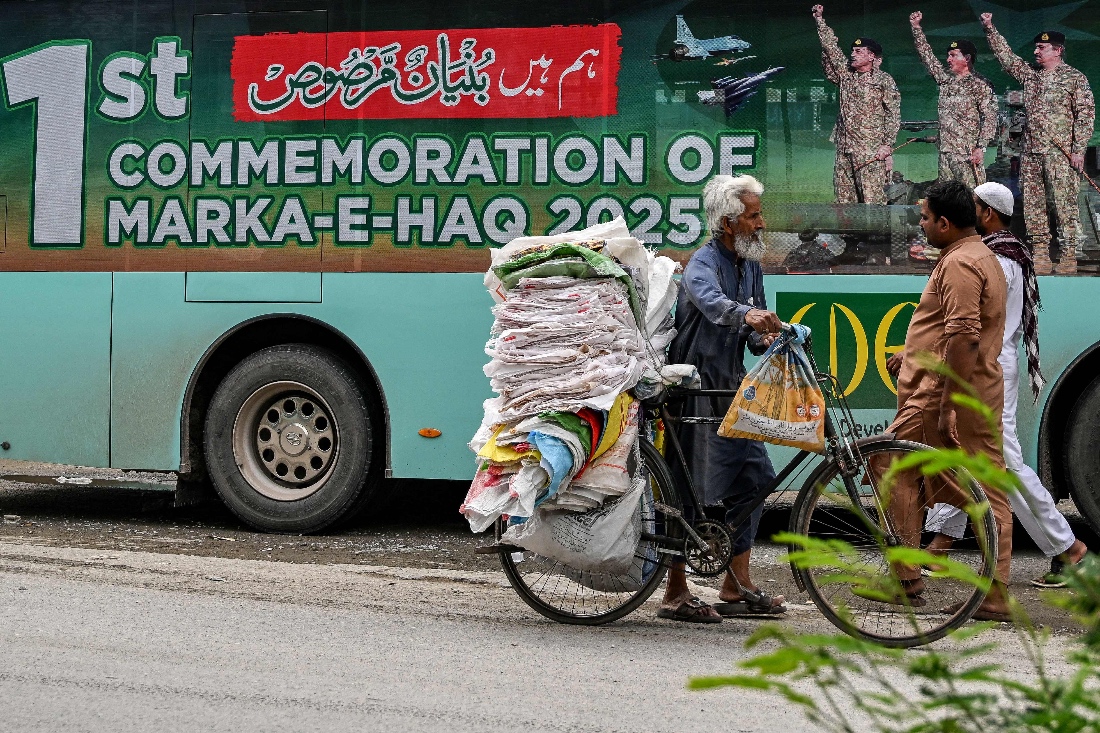 Commuters walk past a government passenger bus carrying a poster of Pakistan's Army Chief and Field Marshal Syed Asim Munir in Islamabad, Pakistan. (AFP)