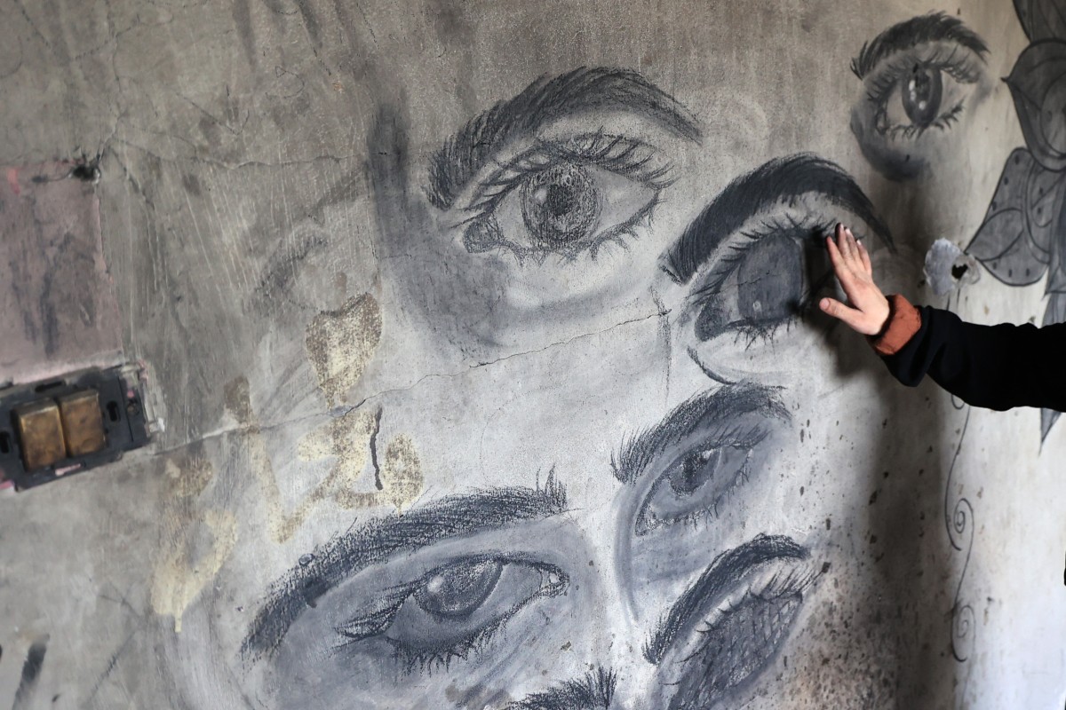 Areej al-Saafin, who lost one of her eyes as a result of an Israeli military strike, touches one of her charcoal drawings on the wall of her home in the Bureij Palestinian refugee camp in the central Gaza Strip, May 2, 2026. (AFP)