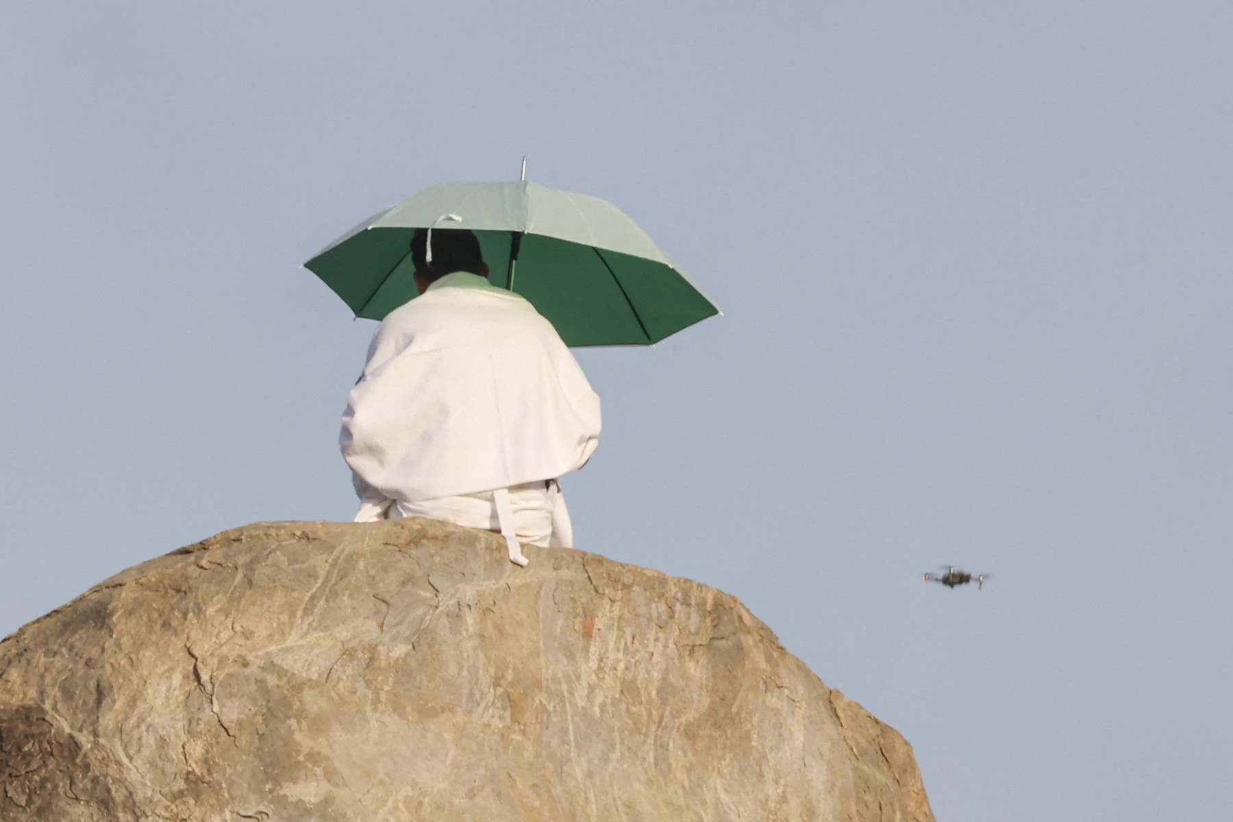 A surveillance drone flies past a Muslim pilgrim as he prays at dawn on Mount Arafat during the climax of the Hajj pilgrimage, June 5, 2025. (Files / AFP)