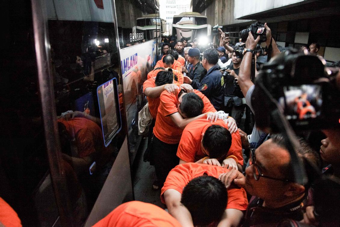 Suspected online gambling operators walk toward buses for transfer after a police raid at the Hayam Wuruk Plaza office building in Jakarta on May 10, 2026. (AFP)