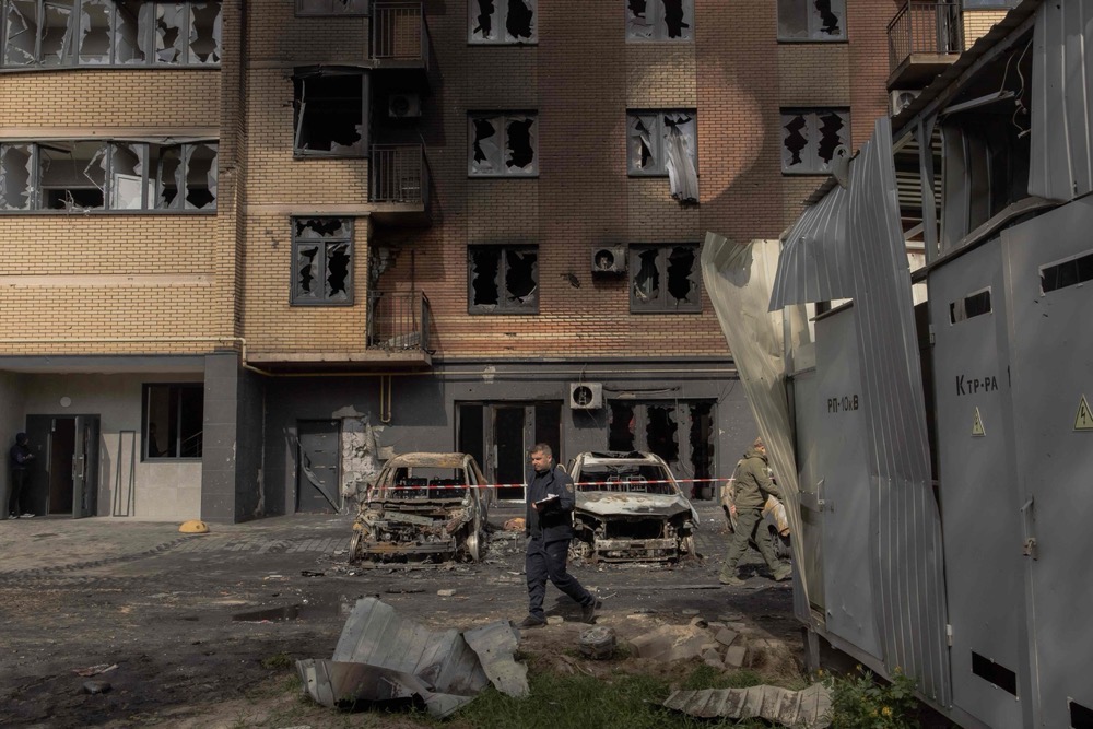 A member of the State Emergency Service of Ukraine walks next to burned cars and a damaged residential building following Russian drone and missile strikes in Kyiv. (AFP)