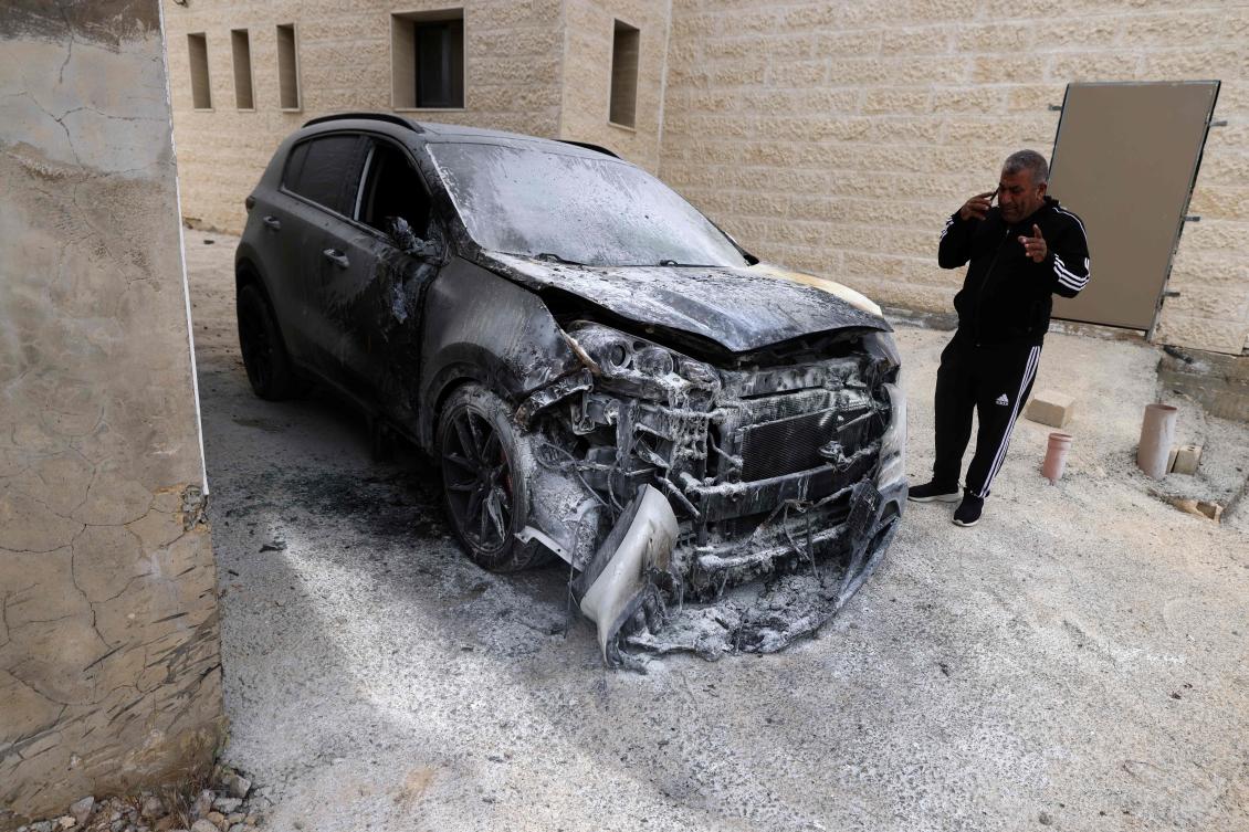 A Palestinian man speaks on his mobile phone as he inspects a destroyed vehicle after Israeli settlers reportedly set fire to it and the basement of a local mosque daubing Hebrew slogans on its external wall, in the village of Jibya, west of the Israeli-occupied West Bank city of Ramallah on May 15, 2026. (Photo by JAAFAR ASHTIYEH / AFP)