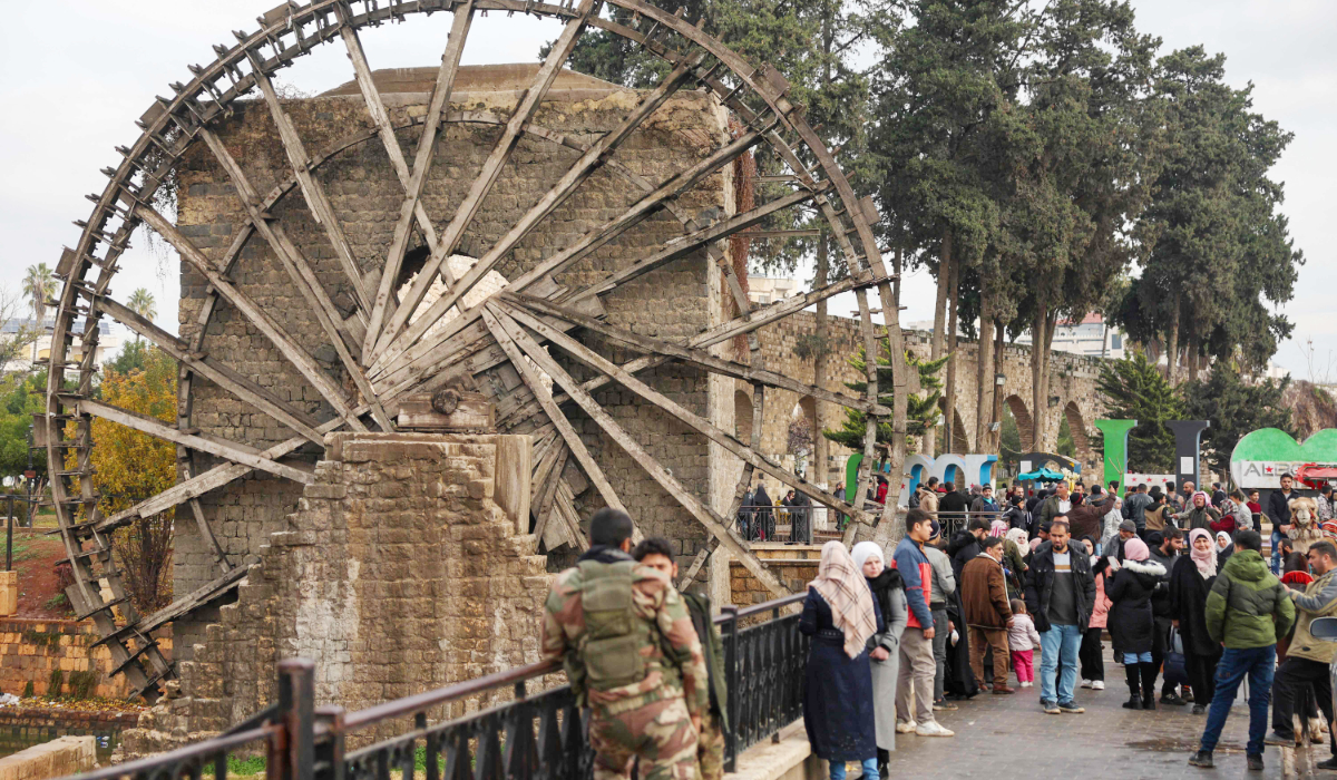 People gather next to a camel near one of Hama's landmark historic water wheels, or norias, on the Orontos riverbank in the heart of the central Syrian city on December 30, 2024. (AFP)