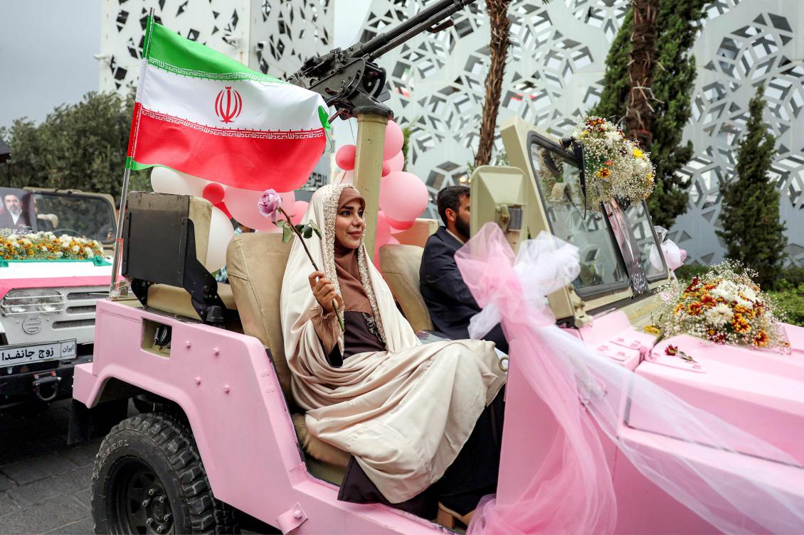 A bride and group couple rides in a military jeep arriving for a public mass wedding ceremony at Imam Hossein Square in Tehran on May 18, 2026. (AFP)