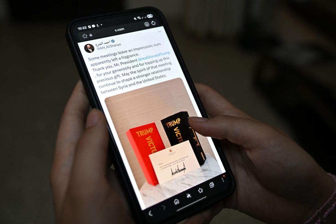 This photo illustration taken in Damascus on May 20, 2026 shows the X account of Syrian President Ahmed Al-Sharaa on a smartphone displaying his tweet on thanking US President Donald Trump for a gift of Trump cologne. (AFP)