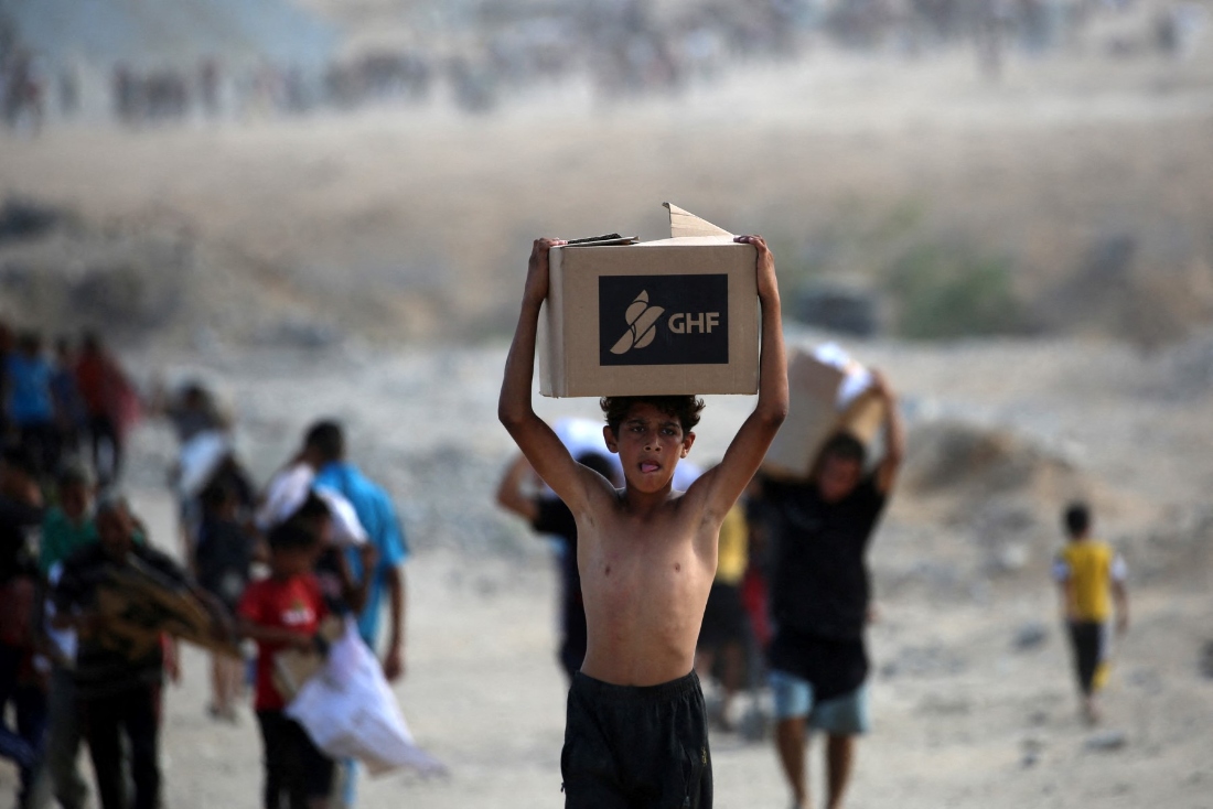 A Palestinian boy carries a box as people return from a food distribution point run by the US and Israeli-backed Gaza Humanitarian Foundation (GHF) group, near the Netsarim corridor in the central Gaza Strip. (AFP)