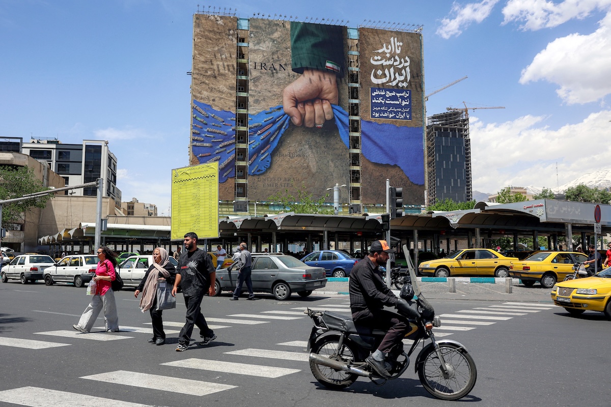 A motorist rides a scooter along a street near a billboard on the facade of a building depicting the Strait of Hormuz with a caption in Persian reading "Forever in Iran’s Hand", at Vanak Square in Tehran on May 6, 2026. (FILE/AFP)
