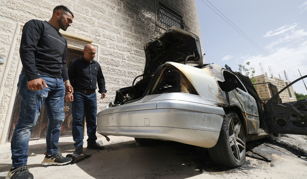 Palestinians inspect destroyed vehicles outside their home hours after Jewish settlers allegedly set fire to two vehicles and scrawled Hebrew graffiti on the walls in Halhul, five kilometres north of the Israeli-occupied West Bank city of Hebron, on May 20, 2026. (AFP)