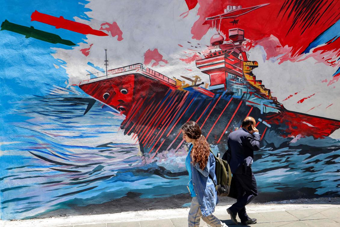 People walk past an anti-US and anti-Israel mural depicting missiles hitting an aircraft carrier in Tehran on Tuesday. US forces launched overnight strikes on missile sites in Iran and boats. (AFP)