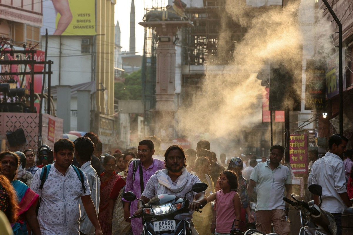 People walk under water sprinklers installed along a street on a hot summer day in Varanasi, India. (AFP)