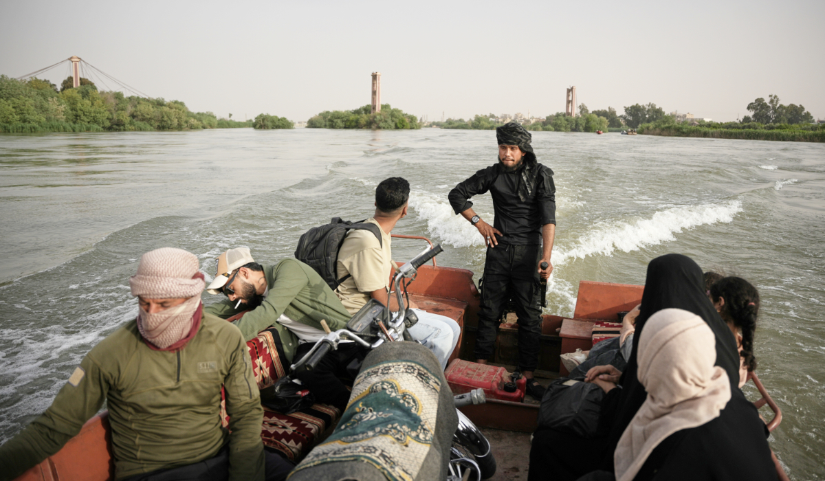 Residents travel by boat along the flooded Euphrates River near Deir ez-Zor, Syria, Thursday, May 28, 2026, as damaged bridge structures are seen in the background. (AP)