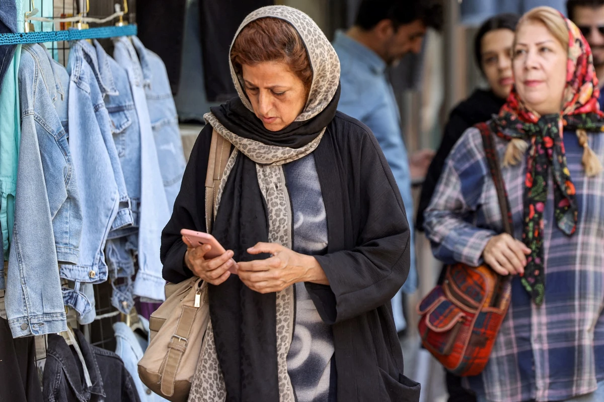 A woman browses a phone while walking along a street in Tehran, Iran. (AFP)