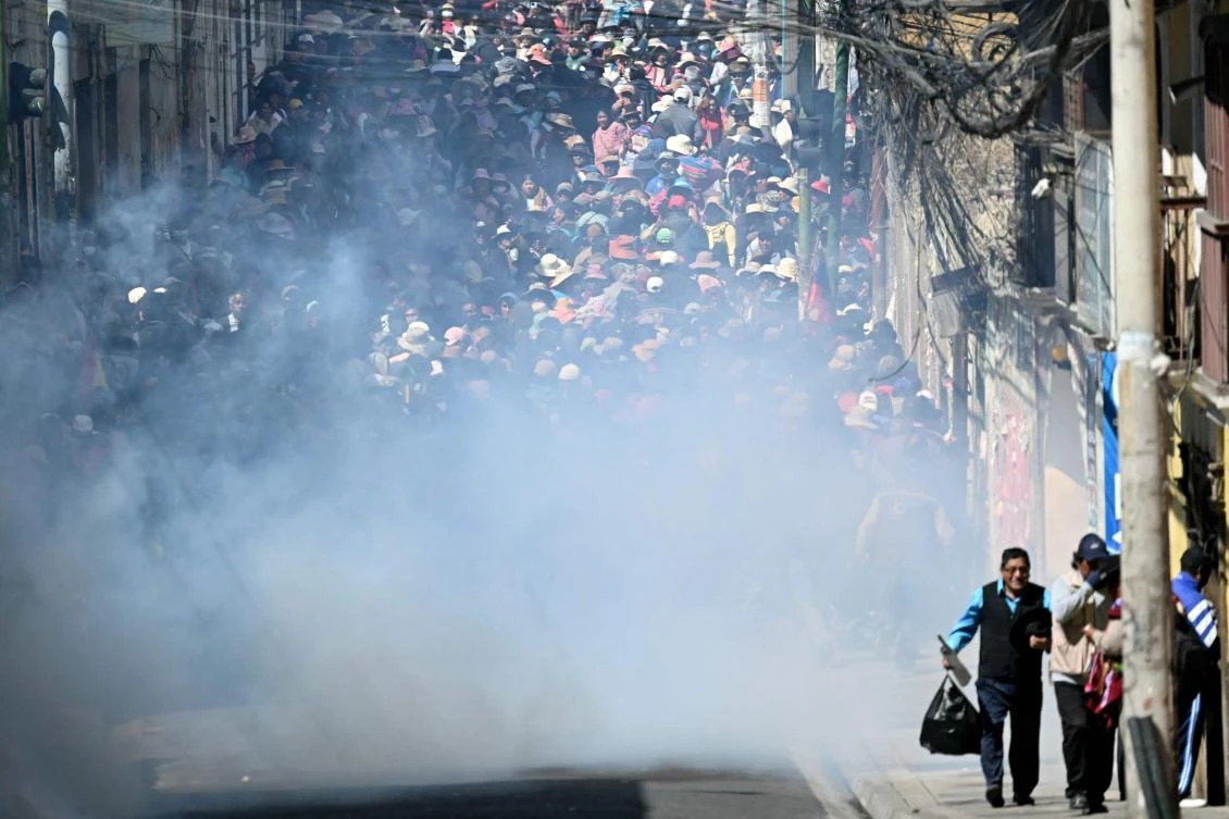 Protesters run to escape tear gas during clashes with riot police in a protest demanding the resignation of Bolivian President Rodrigo Paz, in La Paz, on May 18, 2026. (AFP)