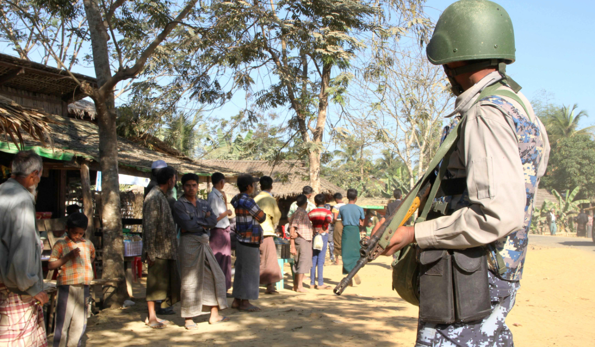 A Myanmar border guard policeman stand near a group of Rohingya Muslims in front of their homes in the restive Rakhine state. (