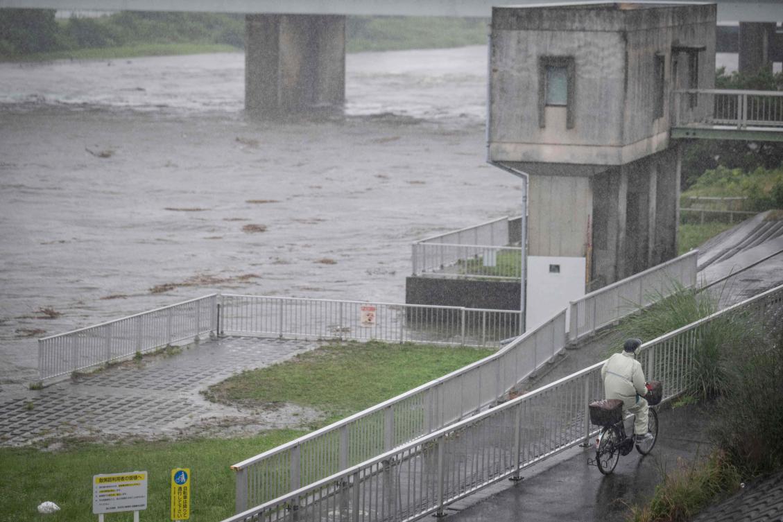A man cycles past the Tama river amid heavy rain brought by severe tropical storm Jangmi in Tokyo on June 3, 2026. (AFP)