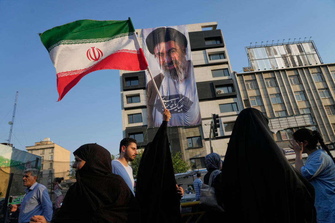 A woman holds up an Iranian flag in front of a banner showing a portrait of the Supreme Leader Ayatollah Mojtaba Khamenei in Tehran on Thursday. (AP)