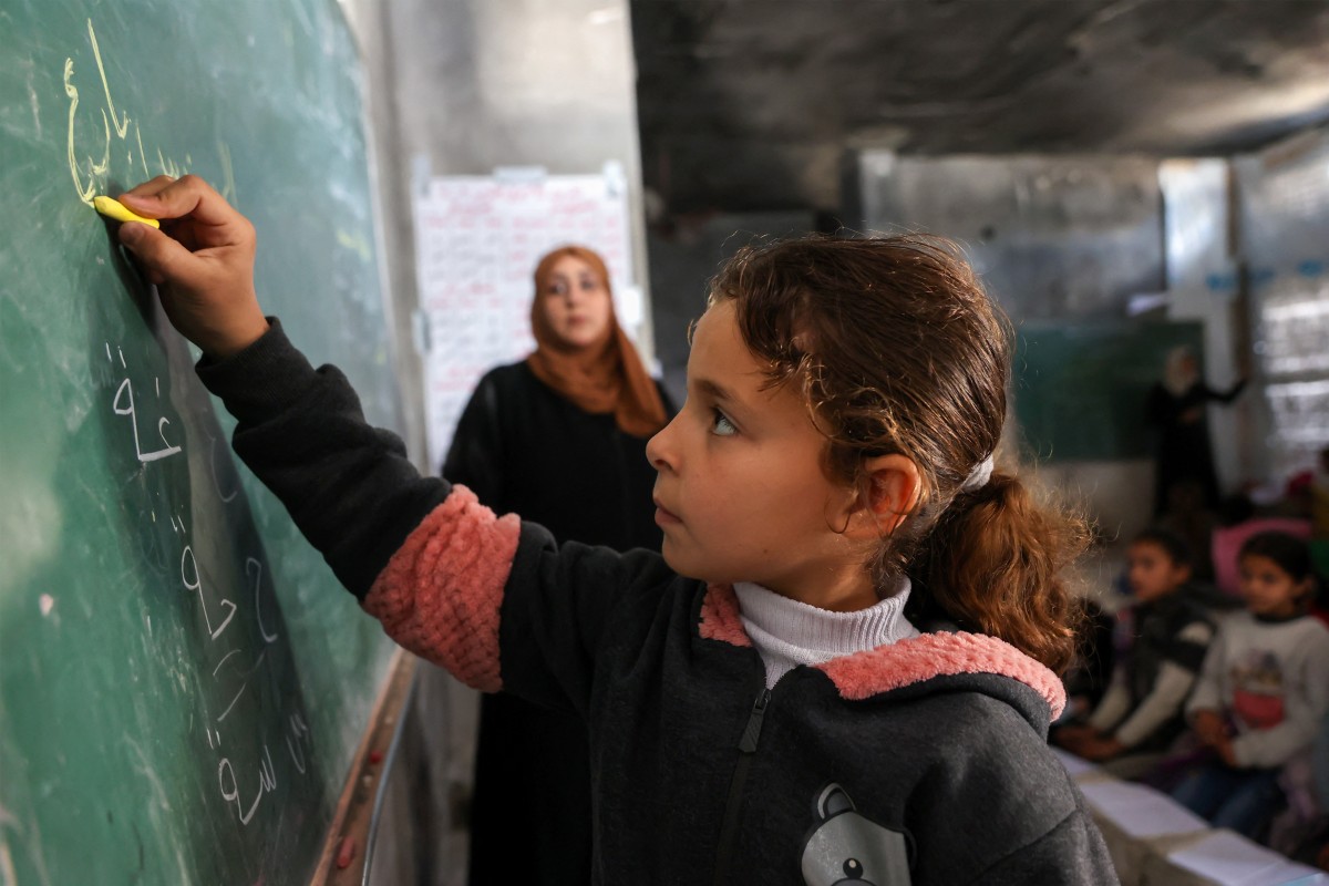 A displaced Palestinian child writes on a blackboard during class inside a tent at the Mada Educational School in the Jabalia refugee camp in the northern Gaza Strip, Apr. 13, 2026. (AFP)