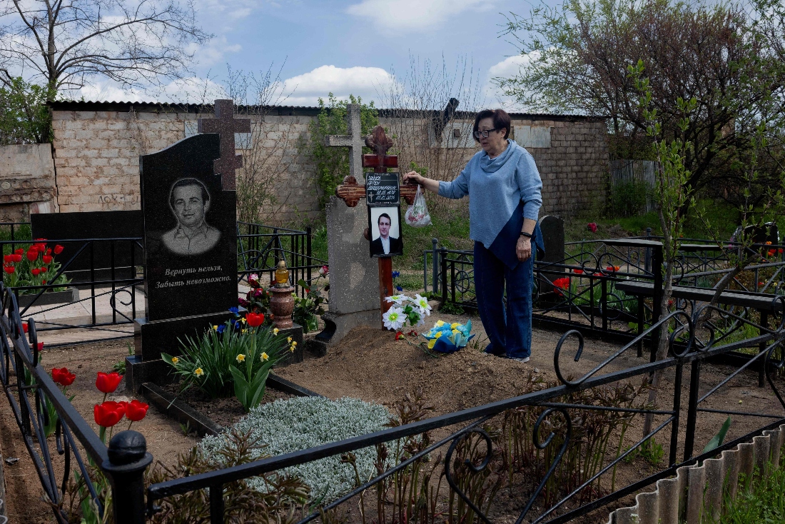 Tetiana Zaitseva whose son Artem Zaitsev died after being detained at a territorial recruitment centre during the night of May 4 and 5, 2024, stands at the side of her son's grave in Kryvyi Rig, Ukraine. (AFP)