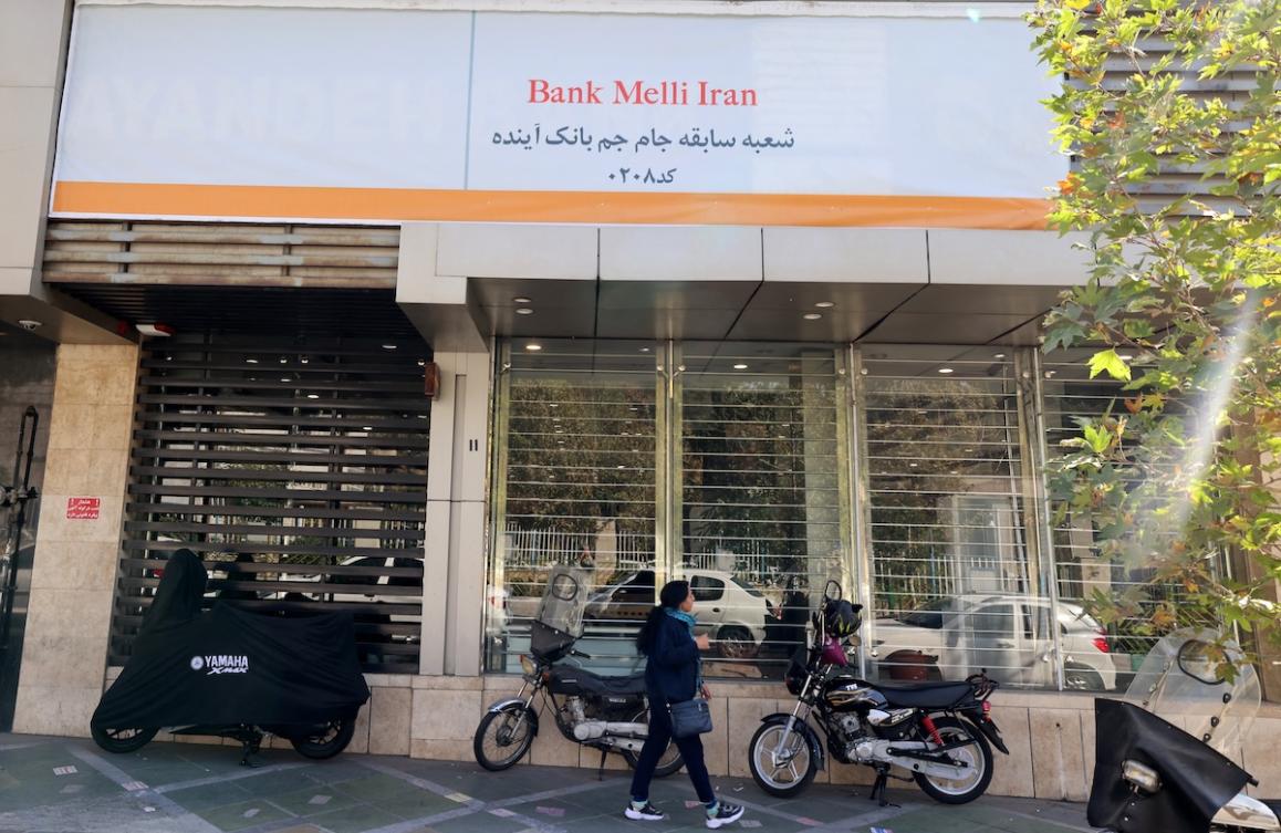 An Iranian woman walks past a branch of the state-owned Melli Bank, which absorbed the assets of the now-defunct Ayandeh Bank. (FILE/AFP)