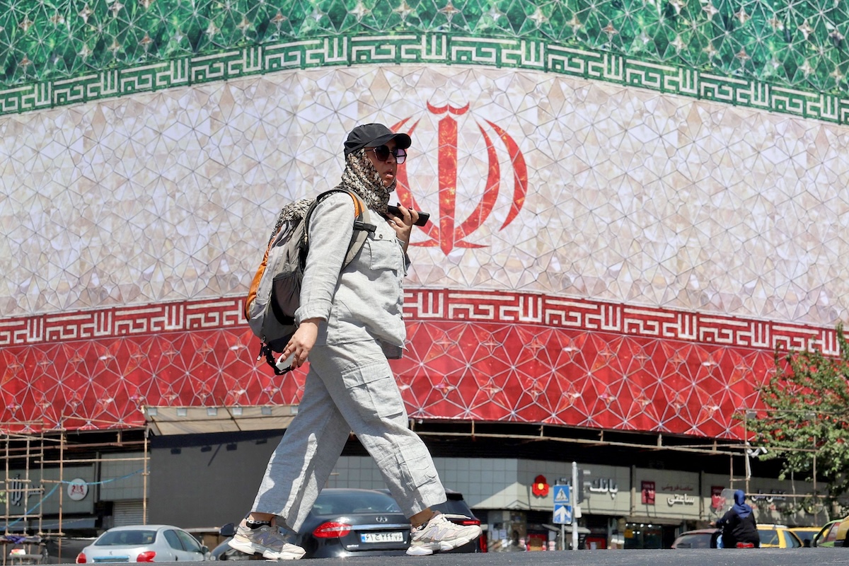 A woman walks past a billboard displaying Iran’s national flag at Enghelab Square in Tehran on June 14, 2026. (File/AFP)