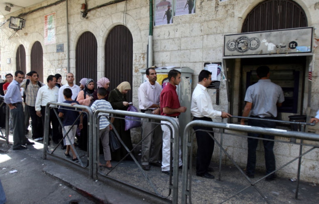 Palestinian civil servants queue at an electronic cash point machine in the occupied West Bank city of Ramallah. (AFP)
