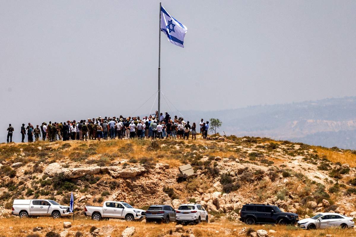 Israeli settlers, accompanied by Israel's far-right finance minister Bezalel Smotrich, raise a large Israeli flag during a cornerstone laying ceremony for a new settlement on Mount Tarousa in occupied West Bank. (AFP)