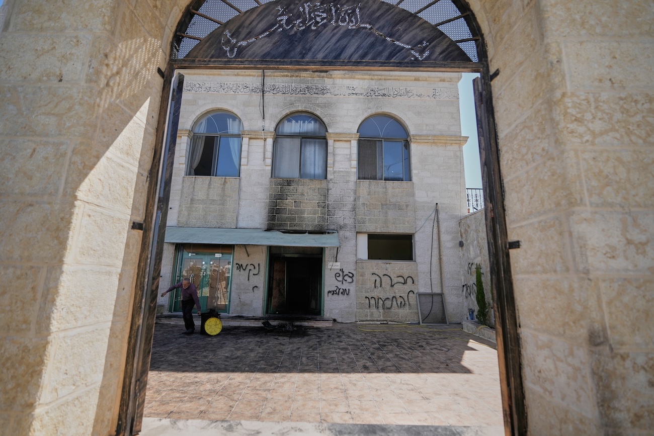 A man clears the rubble as writing in Hebrew on the wall reads “revenge, regards to the arrested, people, wake up,” at one of the West Bank mosques that were vandalized and partly set on fire by Israeli settlers overnight, in the village of Jiljilya, north of Ramallah, Wednesday, June 17, 2026. (AP)
