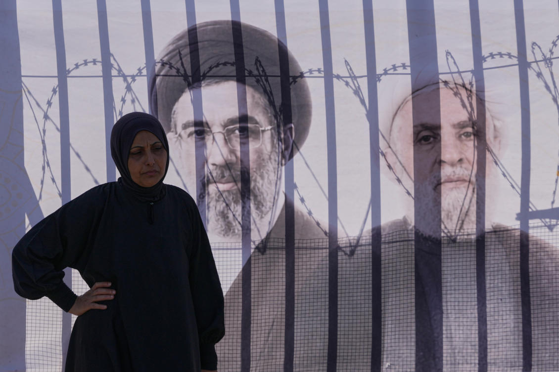 A Hezbollah supporter stands next of a banner that shows portraits of Iran’s Supreme Leader Mojtaba Khamenei, left, and Hezbollah leader Sheikh Naim Qassem. (AP)