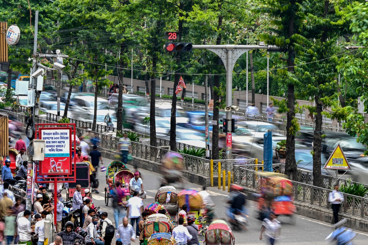This photograph taken on May 14, 2026 shows people travelling past an AI-based traffic management system (L) installed along a road in Dhaka, Bangladesh. (AFP)