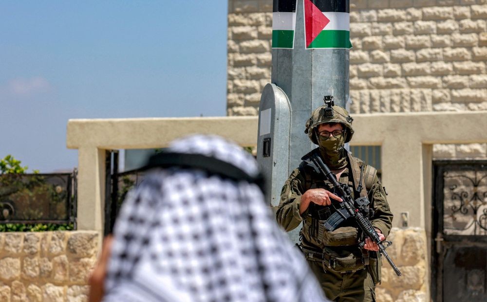 A Palestinian man speaks on a phone near Israeli army soldiers at the archaeological site of Sebastia, north of Nablus, occupied West Bank, June 29, 2026. (AFP)