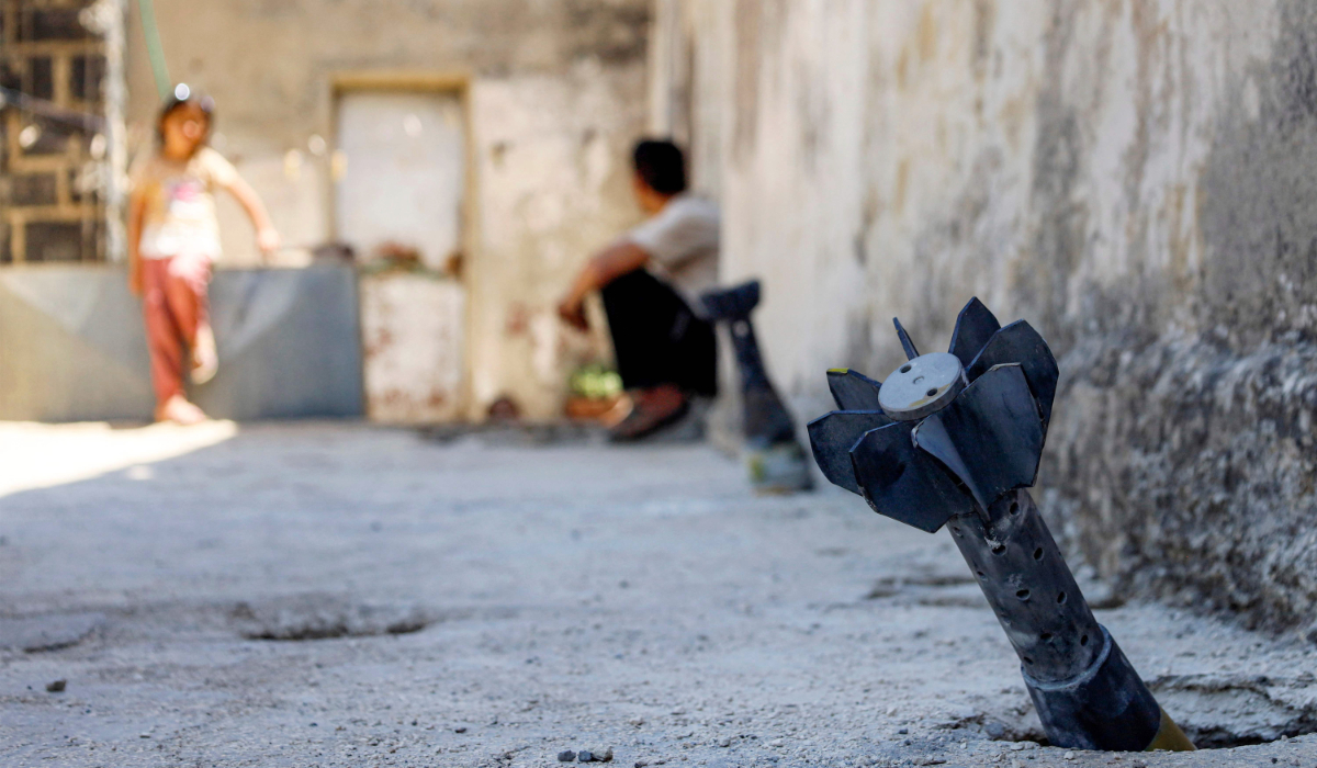 A man speaks with a child while sitting near an unexploded artillery shell that fell during reported overnight Israeli bombardment that hit the village of Abidin in Syria's southwestern Daraa province, close to the Golan Heights, on June 29, 2026. (AFP)