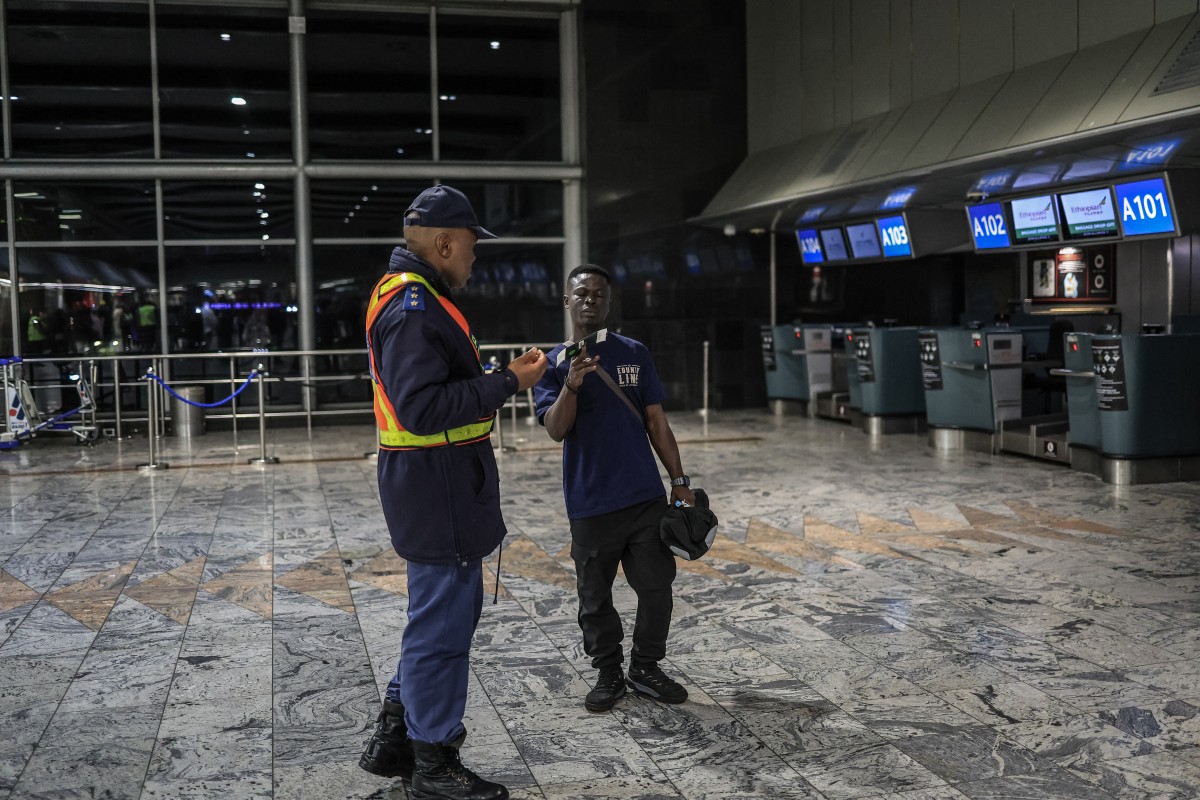 File photo: A Ghanaian national holds his passport and boarding pass as he speaks with a member of the South African Police Service (SAPS) at the check-in desk for an evacuation flight at OR Tambo International Airport in Ekurhuleni on May 27, 2026. (AFP)