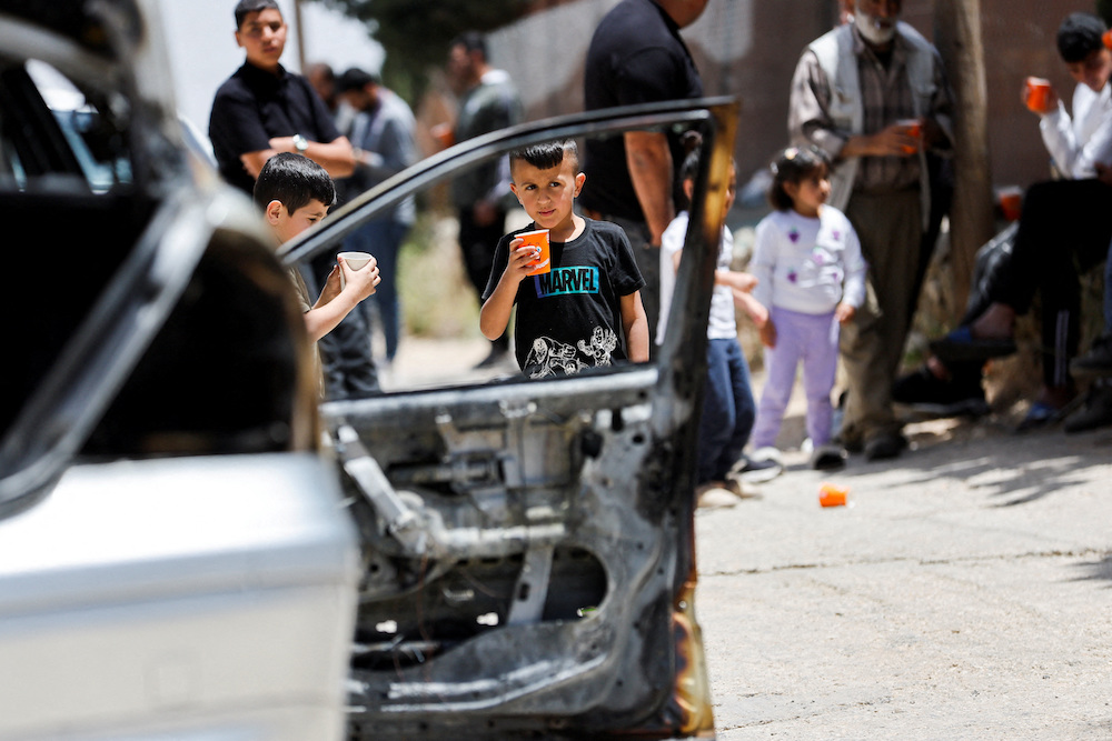 Children stand near a damaged car, which Palestinians say was burned by Israeli settlers,in Halhul near Hebron in the Israeli-occupied West Bank in May. (Reuters/File Photo)