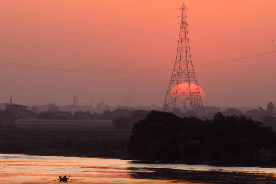 An Egyptian fisherman travels bt boat as the sun is seen behind high-voltage power lines and electricity pylons along the River Nile during a heatwave in Al-Qanatir al-Khairia, on the outskirts of Cairo, Egypt, July 4, 2026. REUTERS/Amr Abdallah Dalsh