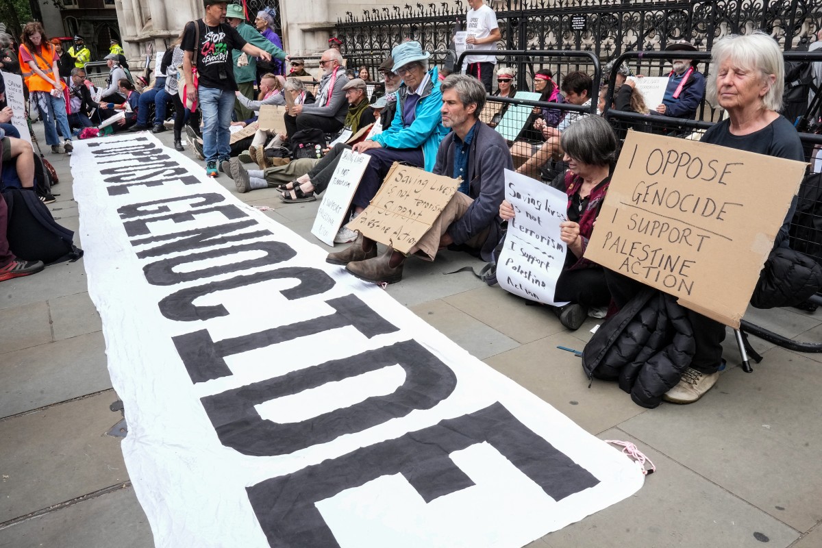 Protesters hold placards as they sit by a banner reading 'I oppose genocide', outside the Royal Courts Of Justice in central London on June 15, 2026. (File/AFP)